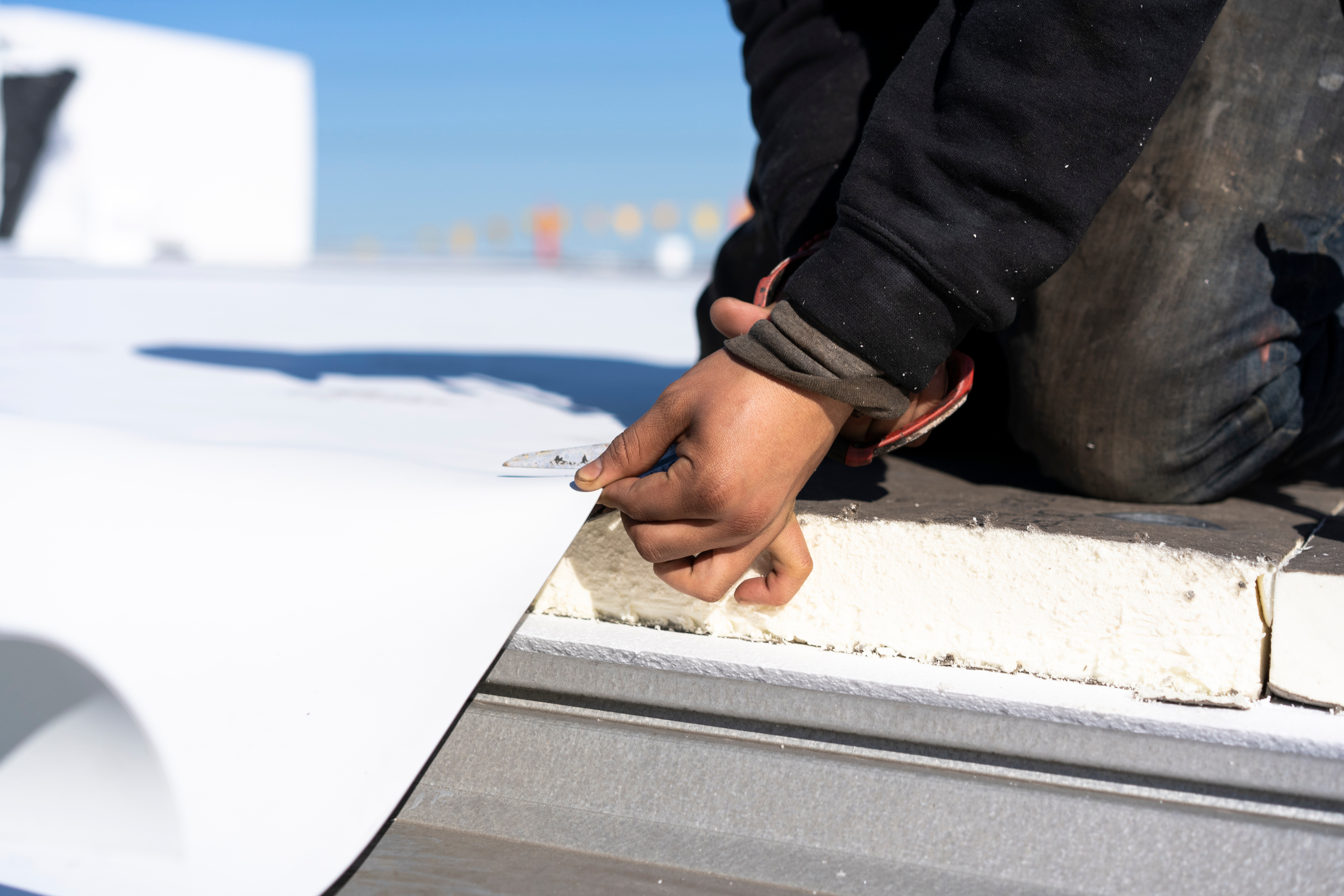hands,of,roofing,construction,worker,cutting,tpo,materials.,bright,blue